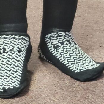 A pair of feet wearing short, black anti-slip socks with white grips on both the top and bottom of the foot.