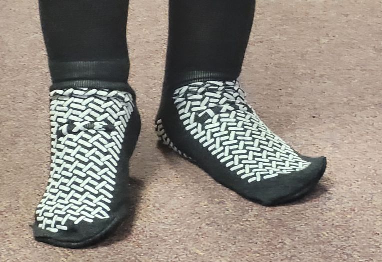 A pair of feet wearing short, black anti-slip socks with white grips on both the top and bottom of the foot.