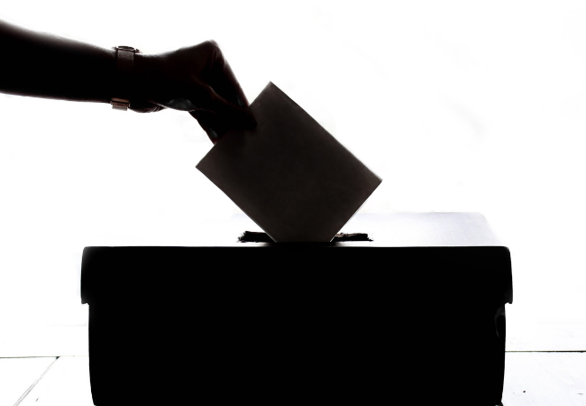 A silhouetted photograph of a hand putting a vote into a ballot box